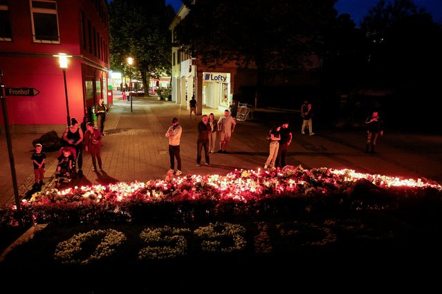 People stand in front of flowers and candles, laid at a makeshift memorial near a sign marking city's 650th anniversary, on the day of protests on the streets of Solingen, following a stabbing rampage in the western German city in which several individuals were killed and injured, in Solingen, Germany on August 26, 2024. A 26-year-old Syrian suspect is currently in German police custody. (Photo by Wolfgang Rattay/Reuters)