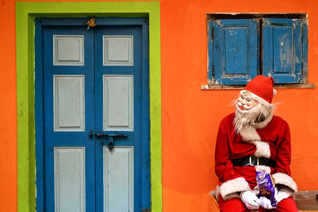 A man dressed in Santa Claus outfit sits outside a house as he waits for passersby to distribute chocolates ahead of Christmas in Chennai, on December 24, 2024. (Photo by R.Satish Babu/AFP Photo)