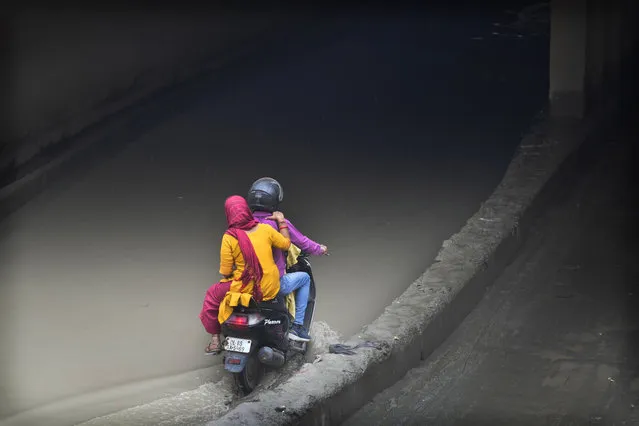 A family on a motorcycle prepare to cross an underpass filled with silt and flooded water from a swollen river Yamuna following excessive rains, in New Delhi, India, Wednesday, July 26, 2023. (Photo by Manish Swarup/AP Photo)