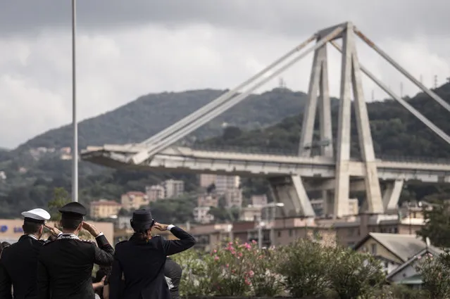 Member of the Italian Police pay tribute to the victims during a minute of silence and a commemoration ceremony near the bridge's wreckage, one month after the Morandi Bridge collapse that killed 43 people, on September 14, 2018 in Genoa. A month after Genoa's Morandi Bridge collapse killed 43 people, the port city is tending to its wounds and those left homeless by the disaster are turning a brave face to the future. (Photo by Marco Bertorello/AFP Photo)