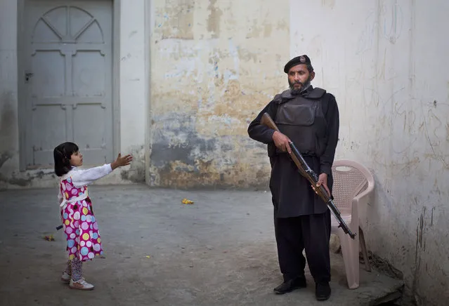 In this Wednesday, November 15, 2012 file photo, a young girl in her colorful dress reaches out to greet a Pakistani policeman securing the road outside Kainat Riaz's home in Mingora, Swat Valley, Pakistan. (Photo by Anja Niedringhaus/AP Photo)