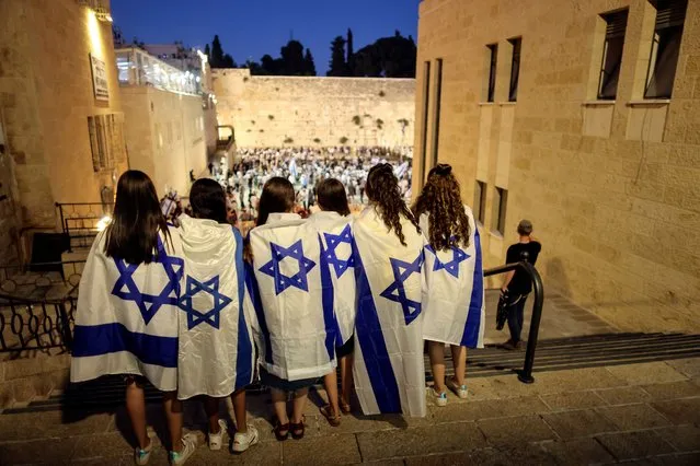 Israeli women cover themselves with Israeli national flags as they stand opposite to the Western Wall, Judaism's holiest prayer site in Jerusalem's Old City on June 15, 2021. (Photo by Ronen Zvulun/Reuters)