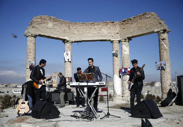 An Afghan band performs at the ruins of Darul Aman palace in Kabul during a campaign called “One Thousand Smiles for Peace” by Non-Violent World Organization (NVWO) February 2, 2016. A military helicopter flies on the left. (Photo by Ahmad Masood/Reuters)