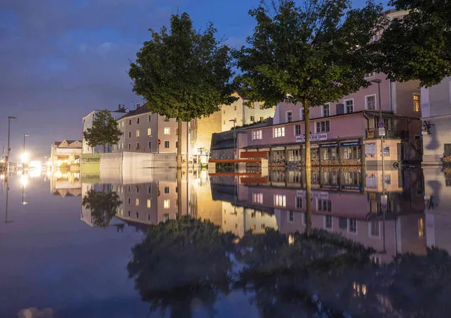 Buildings near the banks are reflected in the evening by floodwaters of the Danube River, which already cover the Promenadenstrasse in Passua, Germany, Sunday, July 18, 2021. (Photo by Peter Kneffel/dpa via AP Photo)