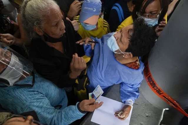 A healthcare worker takes the names of residents gathered outside a vaccination center hoping to be inoculated with a second dose of the Sputnik V COVID-19 vaccine, in Caracas, Venezuela, Thursday, September 16, 2021. The Venezuelan government is beginning rollouts of second doses following months of delays. (Photo by Ariana Cubillos/AP Photo)