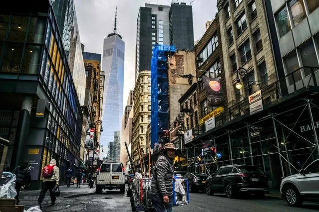 A woman pushes a cart of cleaning supplies in a street of the Manhattan borough of New York on March 20, 2024, as the One World Trade Center building “Freedom Tower” is seen in the background. (Photo by Charly Triballeau/AFP Photo)