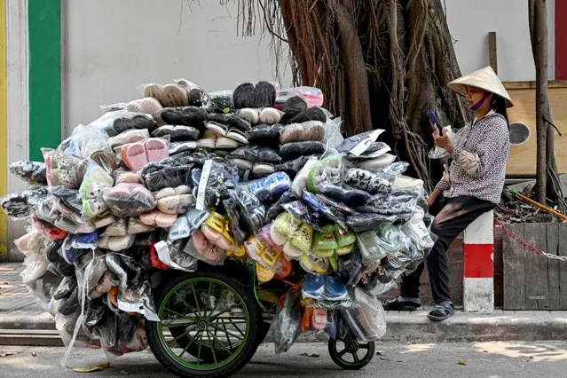 A shoe street vendor uses her phone as she waits for customers along a street in Hanoi on April 3, 2024. (Photo by Nhac Nguyen/AFP Photo)
