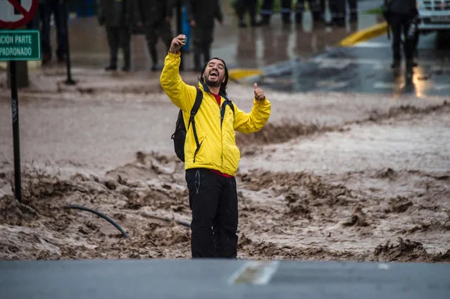 A man takes a selfie next to a flooded street due to the overflowing of the Mapocho river during heavy rains in Santiago on April 17, 2016. Four million people in Santiago were without tap water Sunday after unusually heavy rain pounding central Chile triggered landslides that fouled the city's water supply and forced the closure of the world's biggest copper mine, officials said. (Photo by Martin Bernetti/AFP Photo)