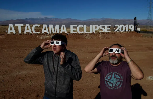 Tourists try special glasses to watch an eclipse at the entrance of an astronomical camp which expects to receive thousands of tourists to observe the July 2 total solar eclipse, in the commune of Vallenar in the Atacama desert about 600 km north of Santiago, on July 1, 2019. A total solar eclipse will be visible from small parts of Chile and Argentina on July 2. (Photo by Martin Bernetti/AFP Photo)