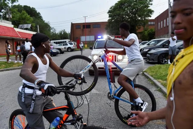 Young people ride their bikes near a police car while they gather in the parking lot of Hip Hop Chicken in Baltimore, Maryland, U.S., May 26, 2019. Each Sunday the bikers gather to ride their bikes and hang out in a loosely affiliated group of bikers. (Photo by Stephanie Keith/Reuters)