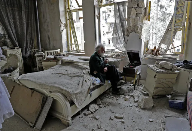 Mohammed Mohiedin Anis, or Abu Omar, 70, smokes his pipe as he sits in his destroyed bedroom listening to music on his vinyl player, gramophone, in Aleppo's formerly rebel-held al-Shaar neighbourhood. (Photo by Joseph Eid/AFP Photo)