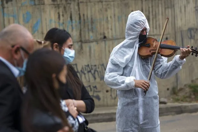 Violinist Antonio Hernandez plays for the relatives of COVID-19 victim Miryam Rodriguez, while they are gathered for prayer by the hearse that carries her remains to Serafin Cemetery, before cremation in Bogota, Colombia, Friday, June 18, 2021. Due to regulations to contain the new coronavirus, relatives cannot enter the cemetery. (Photo by Ivan Valencia/AP Photo)
