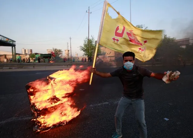 A demonstrator gestures near a burning object at a protest during a curfew, two days after the nationwide anti-government protests turned violent, in Baghdad, Iraq on October 3, 2019. (Photo by Alaa al-Marjani/Reuters)