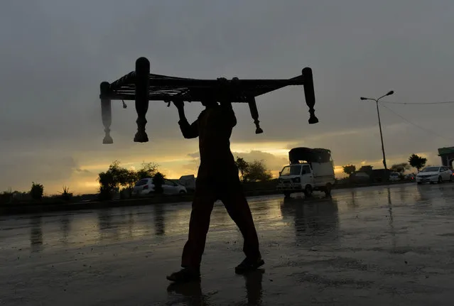 A Pakistani man carries a charpai along a street on a rainy day in Lahore on May 13, 2014. (Photo by Arif Ali/AFP Photo)
