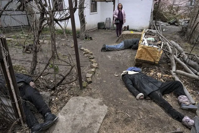 A woman stands next to three people killed in the courtyard of a house in Bucha, on the outskirts of Kyiv, Ukraine, Tuesday, April 5, 2022. (Photo by Rodrigo Abd/AP Photo)