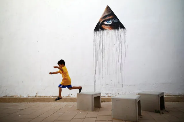 A boy plays in front of a wall painting by Hawaiian artist Kamea Hadar during an art happening, called POW! WOW! Israel, which is connected to a week-long art and culture festival held in Hawaii called POW! WOW! Hawaii, in the southern city of Arad, Israel June 6, 2017. (Photo by Amir Cohen/Reuters)