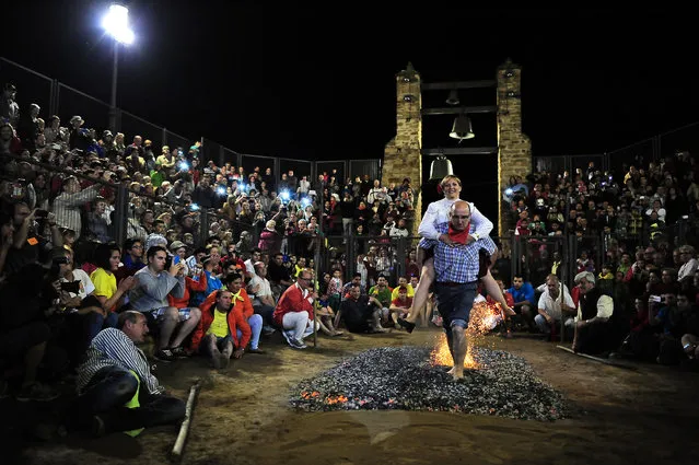 A man carries a woman on his back as she reacts while he walks on burning embers during the night of San Juan, in San Pedro Manrique, northern Spain on Tuesday, June 24, 2014. The night of San Juan, which welcomes the summer season, is an ancient tradition celebrated every year in various towns in Spain. (Photo by Alvaro Barrientos/AP Photo)