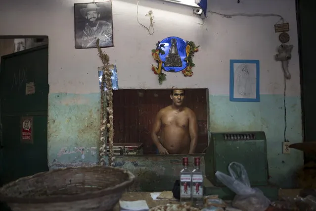 A photograph of Cuba's late rebel revolutionary Camilo Cienfuegos decorates a wall inside a state run market as Osmani Aguilar, 39, waits for customers in Havana, July 20, 2015. (Photo by Alexandre Meneghini/Reuters)