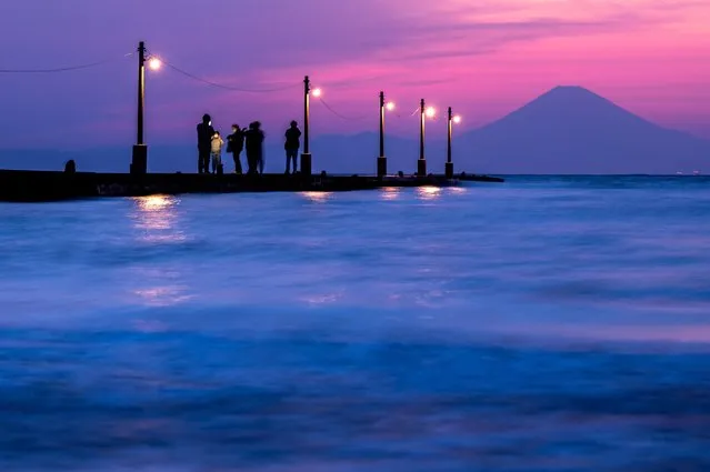 This long exposure picture shows people walking on the Haraoka Pier as Mount Fuji (R), Japan's highest mountain at 3,776 meters, looms from Haraoka Beach of Minamiboso, Chiba prefecture during the “golden week” holiday on May 4, 2022. (Photo by Philip Fong/AFP Photo)