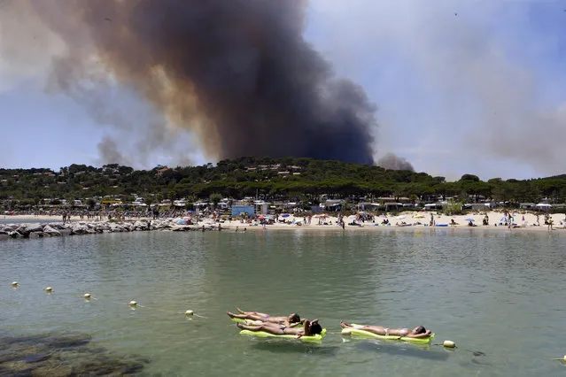 Women enjoy sunbathing in Lavandou, French Riviera, as plumes of smoke rise in the air from burning wildfires, Wednesday, July 26, 2017. Authorities ordered the evacuation of 10,000 people as fires hopscotched around the Riviera for a third day Wednesday, tearing through the forest of La Londe-les-Maures. (Photo by Claude Paris/AP Photo)