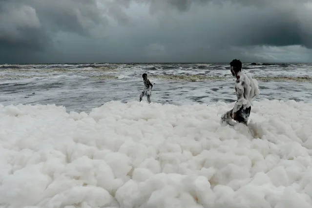 Residents play over foamy discharge, caused by pollutants, as it mixes with the surf at Marina beach in Chennai on December 1, 2019. (Photo by Arun Sankar/AFP Photo)