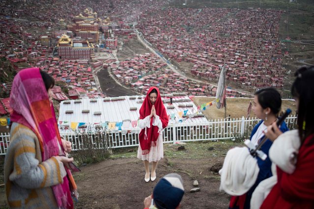 This picture taken on May 29, 2017 shows Chinese tourists posing for a picture overlooking partially demolished houses at the Larung Gar Buddhist Institute in Sertar county in southwest China's Sichuan province. Thousands of monks, nuns and laypeople – including many Han Chinese devotees – crowd this remote valley in Sichuan province to study at Larung Gar, the world's largest and most important institution for Tibetan Buddhist learning. But authorities have ordered the mass expulsion of devotees back to their place of origin, warning that the area is dangerously overcrowded. (Photo by Johannes Eisele/AFP Photo)