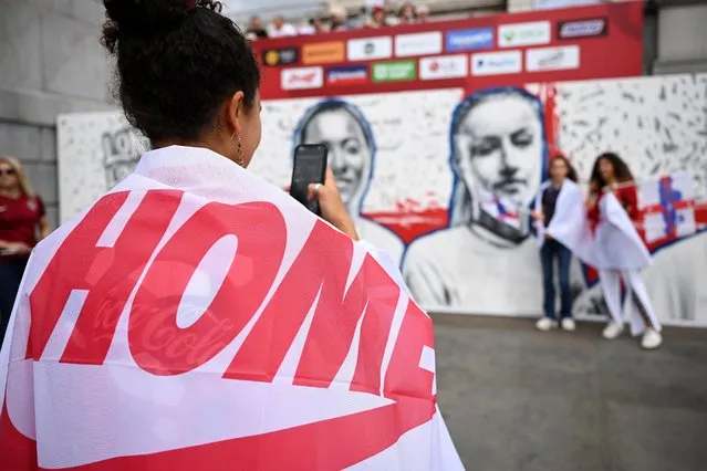 A Fan of England takes a photograph of friends in front of a mural of Fran Kirby and Leah Williamson (not pictured), whilst wearing a Nike Coming Home Flag, during the England Women's Team Celebration at Trafalgar Square on August 01, 2022 in London, England. The England Women's Football team beat Germany 2-1 in the Final of The UEFA European Women's Championship last night at Wembley Stadium. (Photo by Leon Neal/Getty Images)