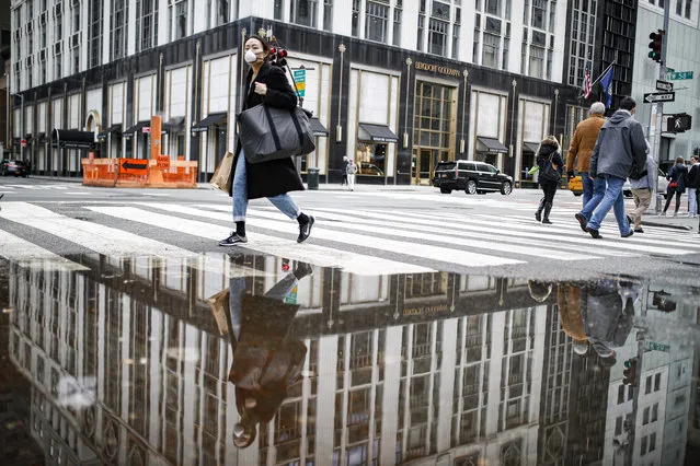 A pedestrian wearing a protective face mask is reflected in a rain puddle, Tuesday, March 17, 2020, in New York. New York state entered a new phase in the coronavirus pandemic this week, as New York City closed its public schools, and officials said schools statewide would close by Wednesday. New York joined with Connecticut and New Jersey to close bars, restaurants and movie theaters along with setting limits on social gatherings. (Photo by John Minchillo/AP Photo)