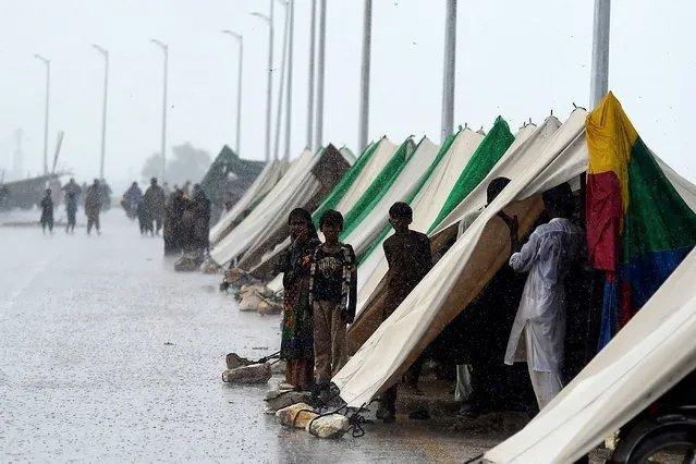 People who fled their flood hit homes stand outside temporary tents set along a road during a heavy monsoon rainfall in Sukkur of Sindh province, on August 27, 2022. (Photo by Asif Hassan/AFP Photo)