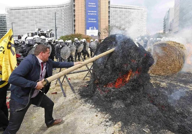 Belgian riot police officers stand guard while protesters push a burning hay ball as farmers and dairy farmers from all over Europe take part in a demonstration outside an European Union farm ministers emergency meeting at the EU Council headquarters in Brussels, Belgium, September 7, 2015. (Photo by Yves Herman/Reuters)