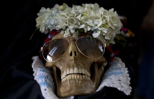 In this Wednesday, November 8, 2017 photo, a human skull wearing sun glasses and flowers is displayed during the Natitas Festival outside the General Cemetery chapel in La Paz, Bolivia. Every year, hundreds of Bolivians carry human skulls adorned with flowers to a cemetery in La Paz, asking for money, health, and other favors as part of a festival. (Photo by Juan Karita/AP Photo)