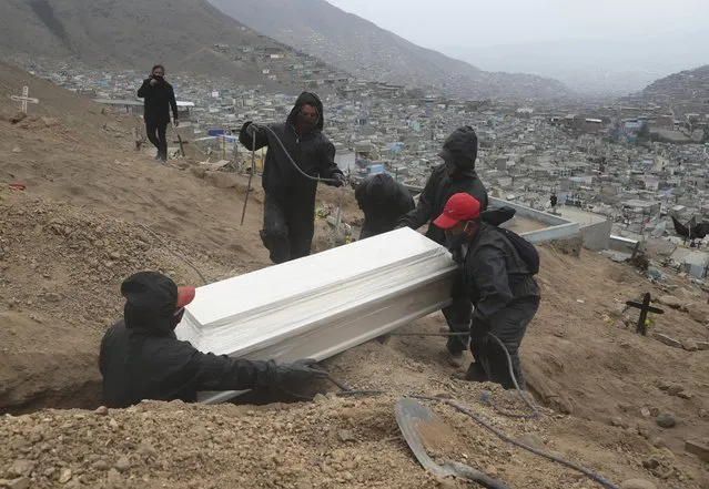 Cemetery workers  place into a grave the coffin that contains the remains Juliana Ramos at the Martires 19 de Julio cemetery, on the outskirts of Lima, Peru, Wednesday, June 17, 2020. According to the family the 75-year-old woman, who suffered from diabetes, died at hospital after being admitted with symptoms related to the new coronavirus. (Photo by Martin Mejia/AP Photo)