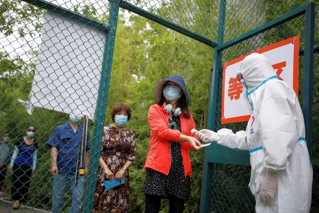 A woman has her body temperature checked as she arrives for a nucleic acid test, during a government-organized visit to a testing site, following a new outbreak of the coronavirus disease (COVID-19) in Beijing, China on June 24, 2020. (Photo by Carlos Garcia Rawlins/Reuters)