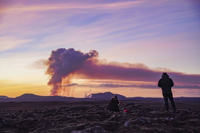 People watch from the north as the volcano erupts near Grindavík, Iceland, Sunday January 14, 2024. A volcano has erupted in southwestern Iceland, sending semi-molten rock spewing toward a nearby settlement for the second time in less than a month. Iceland's Icelandic Meteorological Office says the eruption Sunday came after a swarm of earthquakes near the town of Grindavik. (Photo by Marco Di Marco/AP Photo)