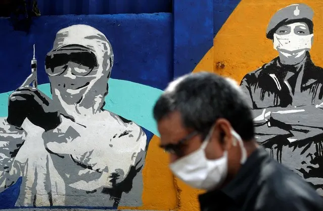 A man wearing a protective mask walks past a graffiti paying tribute to police and healthcare workers during a lockdown to slow the spread of the coronavirus disease (COVID-19) in Mumbai, India June 24, 2020. (Photo by Francis Mascarenhas/Reuters)