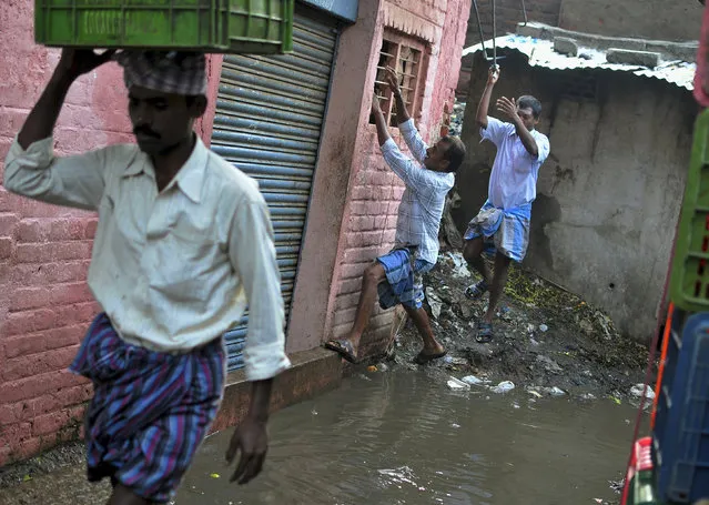 A man holds onto a window grill as he attempts to cross a waterlogged footpath at a market in the southern Indian city of Bangalore October 9, 2014. (Photo by Abhishek N. Chinnappa/Reuters)