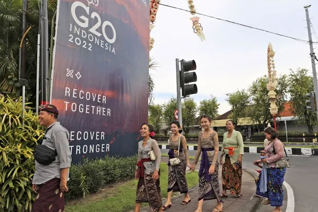 Balinese in traditional dress walk past a G20 banner in Nusa Dua, Bali, Indonesia on Friday, November 11, 2022. A showdown between Presidents Joe Biden and Vladimir Putin isn't happening, but the fallout from Russia's invasion of Ukraine and growing tensions between China and the West will be at the forefront when leaders of the world's biggest economies gather in tropical Bali this week. (Photo by Firdia Lisnawati/AP Photo)