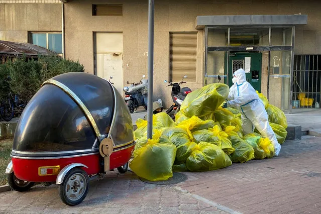 A pandemic prevention worker in a protective suit piles up bags of medical waste outside a building where residents isolate at home as coronavirus disease (COVID-19) outbreaks continue in Beijing on December 5, 2022. (Photo by Thomas Peter/Reuters)