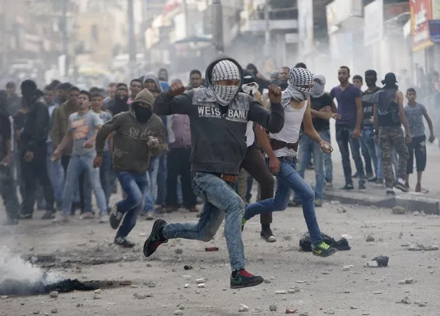 Masked Palestinian protesters run for cover during clashes  with Israeli troops in the West Bank city of Hebron October 9, 2015. (Photo by Mussa Qawasma/Reuters)