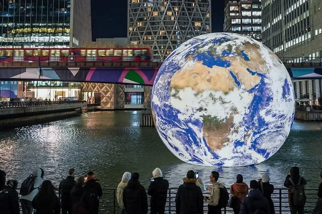 Canary Wharf Winter Lights festival sees Gaia earth installation by Luke Jerram floating in the wharf dock in London, UK on 16th January, 2023. The monumental internally-lit sculpture returns for the popular Winter Lights illuminated installations. UK artist Jerram aims to instil a sense of “overview effect” that astronauts experience when looking down at earth from space. (Photo by Guy Corbishley/Alamy Live News)