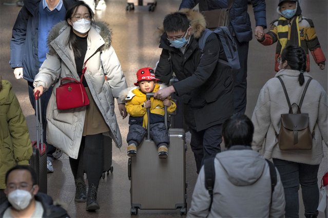 A man pushes a child riding on a suitcase at Beijing West Railway Station in Beijing, Wednesday, January 18, 2023. A population that has crested and is slowly shrinking will pose new challenges for China's leaders, ranging from encouraging young people to start families, to persuading seniors to stay in the workforce longer and parents to allow their children to join the military. (Photo by Mark Schiefelbein/AP Photo)