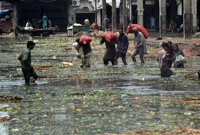 Labourers wade through a flooded fruit and vegetable market after heavy monsoon rains in Lahore on August 10, 2020. (Photo by Arif Ali/AFP Photo)