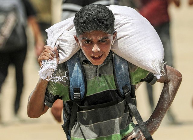 An Palestinian youth carry bag of flour near a food distribution point in Zikim, northern Gaza Strip, 08 August 2025. Humanitarian organizations have warned of an imminent food catastrophe for thousands of children, a crisis caused by severe food insecurity, a decline in health services, and ongoing restrictions on humanitarian aid and essential supplies. (Photo by Mohammed Saber/EPA)