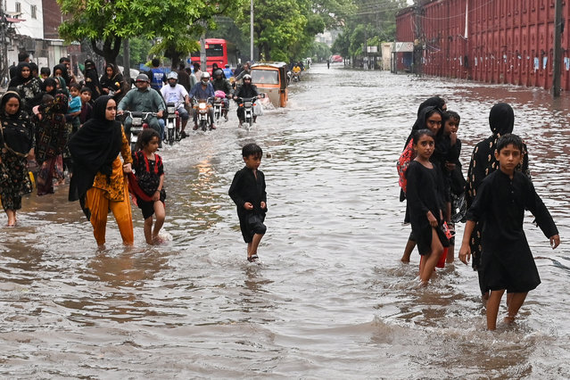 Commuters wade through a flooded street after heavy rainfall in Lahore on July 23, 2025. (Photo by Arif Ali/AFP Photo)