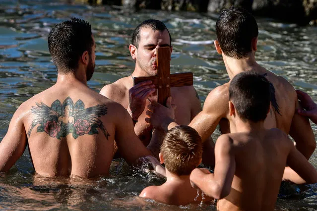 A Greek Orthodox believer, surrounded by faithfuls, kisses a wooden crucifix thrown into the sea during Epiphany Day celebrations, in Piraeus near Athens on January 6, 2022. Similar celebrations for the Epiphany day are held across the country in rivers and lakes. (Photo by Louisa Gouliamaki/AFP Photo)