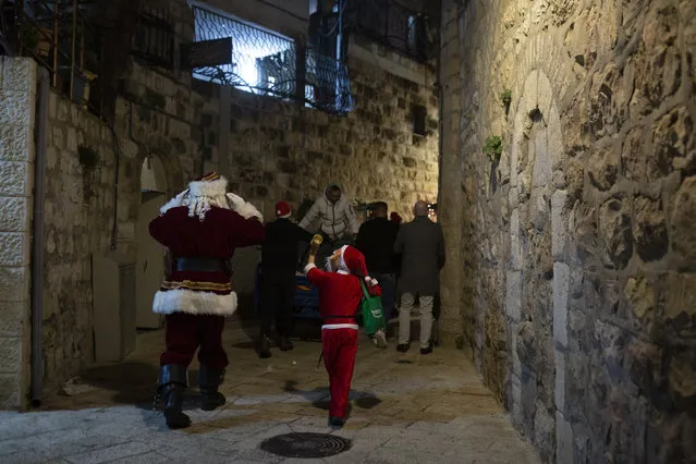 A child dressed as Santa Claus, right, rings a bell for Jerusalem's Santa Claus as they walk with volunteers from a Catholic men's group distributing presents to children on Christmas Eve in the Christian Quarter of the Old City of Jerusalem, Thursday, December 24, 2020.  With the coronavirus dampening Christmas celebrations this year, the men's group organized gifts to families free of charge. (Photo by Maya Alleruzzo/AP Photo)