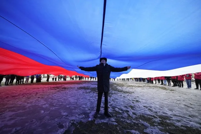A Navy school cadet stands under a giant Russian flag during an action to mark the ninth anniversary of the Crimea annexation from Ukraine, in St. Petersburg, Russia, Saturday, March 18, 2023. (Photo by Dmitri Lovetsky/AP Photo)