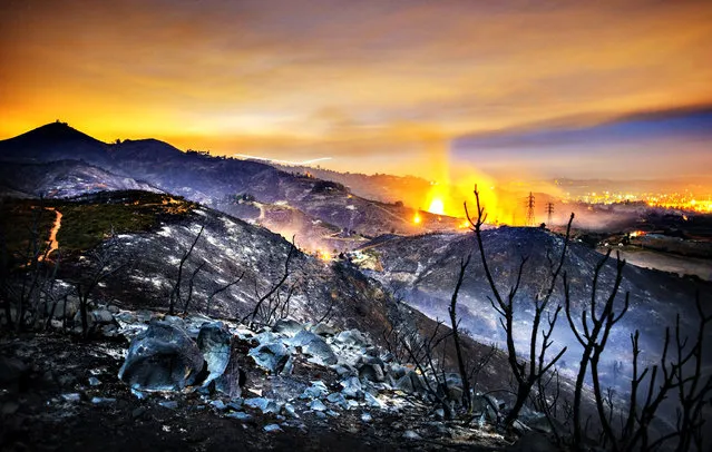 A longtime exposure shows smolderings remains of overnight fires on the hillsides of San Marcos, San Diego county, California, USA, early 16 May 2014. Over 1,000 firefighters battled a series of fast-moving southern California wildfires on 15 May that spread across the region despite the efforts of more than 20 firefighting aircraft. Huge clouds of black smoke hung over much of San Diego County, where the worst blazes were burning 15 May, driven by the blistering Santa Ana winds, which bring strong, dry gusts out from the interior desert. (Photo by Stuart Palley/EPA)