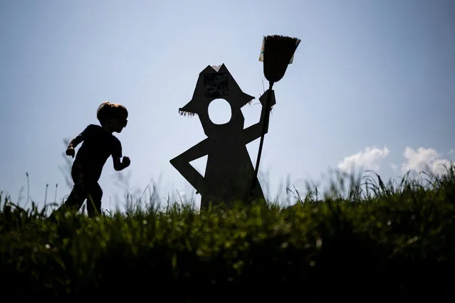 A picture taken on May 22, 2023 shows a child running near a  scarecrow displayed during the annual “Scarecrows Fair” in the Italian northern village of Castellar, near Cuneo. During the annual fair, people exhibit the scarecrow they made in gardens, courtyards, fields or streets. (Photo by Marco Bertorello/AFP Photo)