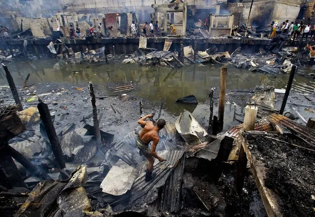 A man tries to retrieve items from still smoldering homes after a fire broke out at a slum area  south of Manila, Philippines, on July 24, 2013. Fire Marshall Major Douglas Guiyab said about 250 houses were gutted in the area and the cause of the fire is still being determined. (Photo by Aaron Favila/Associated Press)